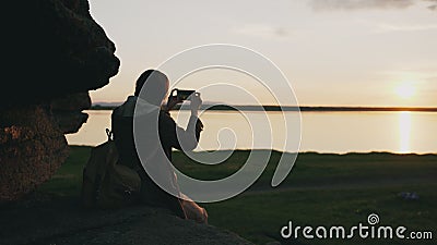 Young tourist woman backpacker photographing landscape on her smartphone camera after hiking on rock at sunset Stock Photo