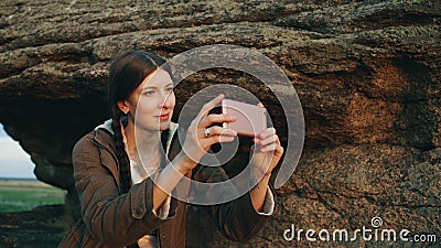 Young tourist woman backpacker photographing landscape on her smartphone camera after hiking on rock at sunset Stock Photo