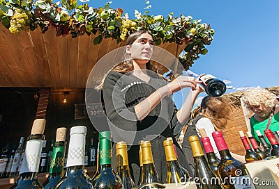 Young trader woman in original dress presents wine for customers, Georgia Editorial Stock Photo