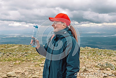Caucasian young blonde girl drinking water from plastic bottle. mountain background. Stock Photo