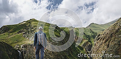 Young Traveler Man Standing On Top Of Cliff In Mountains And Enjoying View Of Nature, Rear View Stock Photo
