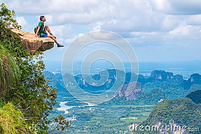 Young traveler sits on a rock that overhangs the abyss, with a beautiful landscape - Khao Ngon Nak Nature Trail in Krabi, Thailand Stock Photo