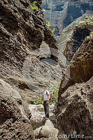 Young traveler stays on the top of huge boulder in the Masca gorge, Tenerife, showing solidified volcanic lava flow layers and Editorial Stock Photo