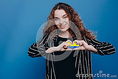 young Ukrainian curly hair woman smiling and showing a heart shape with hands with flag Ukraine Stock Photo