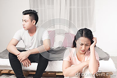 Young Unhappy Asian Couple Sitting Back To Back On Sofa At Home Stock Photo