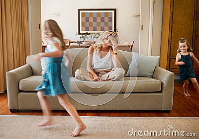 Young unhappy caucasian mother suffering from a headache with her daughters running and playing in the lounge at home Stock Photo