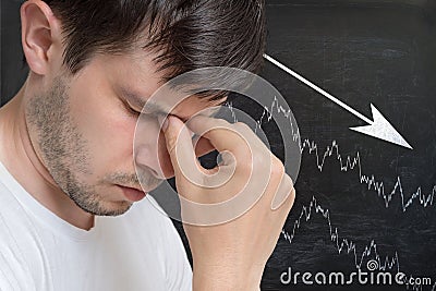 Young unhappy and disappointed man and chart with arrow down on blackboard in background Stock Photo