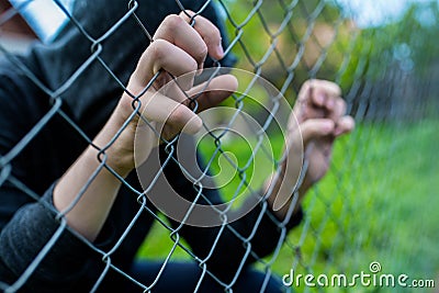 Young unidentifiable teenage boy holding the wired garden at the correctional institute, conceptual image of juvenile delinquency, Stock Photo