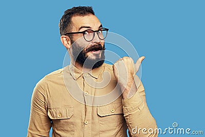 Surprised student man points aside on empty space, isolated over blue wall Stock Photo