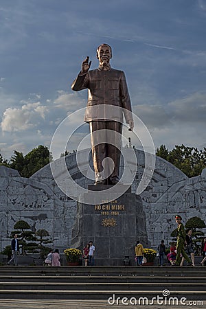 A young Vietnamese soldier armed with a machine gun looks at the camera as he is walking past a huge statue of Ho Chi Minh in Ple Editorial Stock Photo