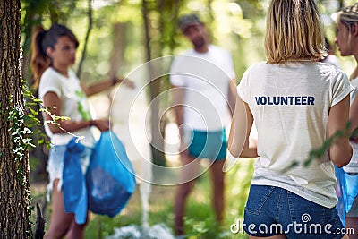 Young volunteers in forest or park, picking up trash. Group of men and women in nature doing charity work. Environmentalism, green Stock Photo