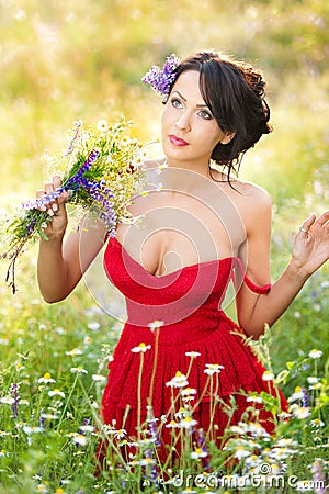 Young voluptuous brunette holding a wild flowers bouquet in a sunny day. Portrait of beautiful woman with low-cut red dress posing Stock Photo