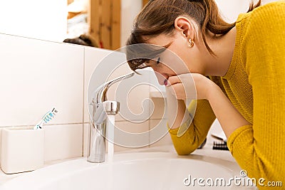 Young vomiting woman near sink in bathroom Stock Photo