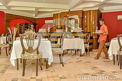 Young waiter in the uniform walking towards table with a tray Editorial Stock Photo