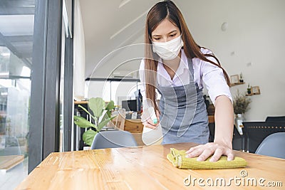 Young waitress with face mask disinfecting restaurant tables Stock Photo
