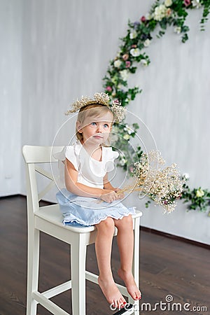 A young warm smiling girl is sitting on the wooden white chair. Stock Photo