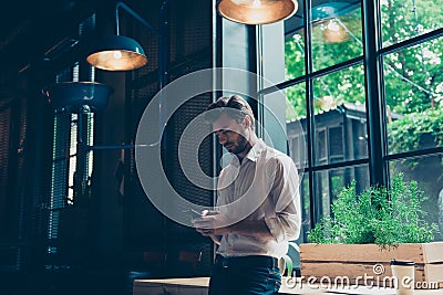 Young well dressed entrepreneur is browsing on his mobile phone at the modern office, behind is a window, he is focused and seriou Stock Photo