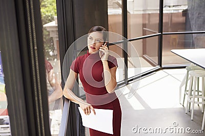 Young white businesswoman on phone looking out office window Stock Photo
