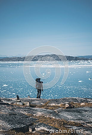 Young white caucasian man with backpack on a hiking trip in Greenland overlooking Atlantic ocean with icebergs. Arctic Stock Photo