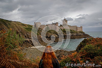 Young white Caucasian woman with long red hair stands against the background of the famous medieval castle la Latte of the fortres Stock Photo