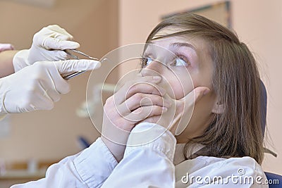 A young white woman in horror looks at the dentist`s hands and tools in her hands. Stock Photo