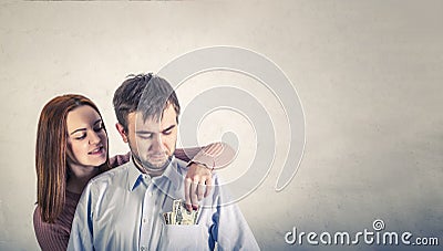 Young wife pulls out dollar bills from her husband`s shirt pocket Stock Photo