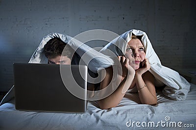 young wife upset unsatisfied and frustrated in bed while husband work on computer laptop ignoring her Stock Photo