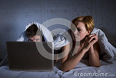 young wife upset unsatisfied and frustrated in bed while husband work on computer laptop ignoring her Stock Photo