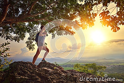 Young woman admires the sunset with a backpack standing on cliff Stock Photo