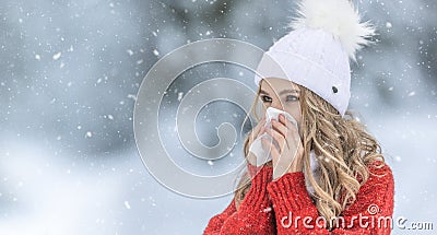 Young woman with allergy symptom blowing nose. A sick girl in a warm knitted sweater and a woolen cap using a tissue in a winter Stock Photo