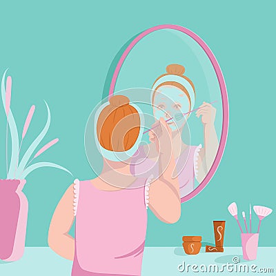 Young woman applies face mask on with brush in front off mirror Stock Photo