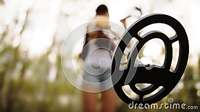 Young woman archeologist using metal detector in the forest. Low angle view. Stock Photo