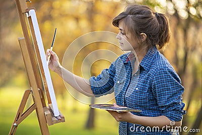 Woman artist drawing a picture on an easel in nature, a girl with a brush and a palette, a concept of creativity and a hobby Stock Photo