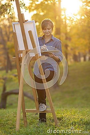 Woman artist drawing a picture on an easel in nature, a girl with a brush and a palette, a concept of creativity and a hobby Stock Photo