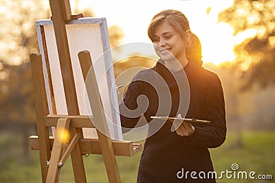 Young woman artist drawing a picture on an easel in nature at sunset in autumn,concept of creativity and a hobby Stock Photo