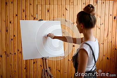 Young woman artist make sketch on canvas on wooden easel. Stock Photo