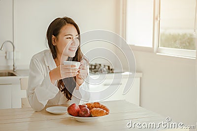 Young woman asia wake up refreshed in the morning and relaxing eat coffee, cornflakes, bread and apple for breakfast at house on h Stock Photo