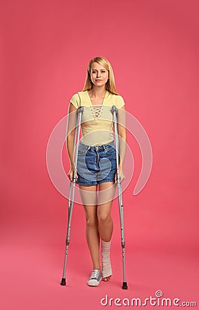 Young woman with axillary crutches on pink background Stock Photo
