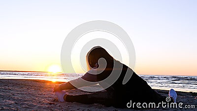 A young woman on the background of the sunset the sun on the seashore does exercises exercised by running, stretching and slumping Stock Photo