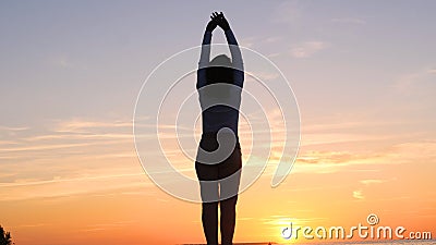 A young woman on the background of the sunset the sun on the seashore does exercises exercised by running, stretching and slumping Stock Photo