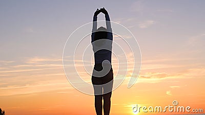 A young woman on the background of the sunset the sun on the seashore does exercises exercised by running, stretching and slumping Stock Photo