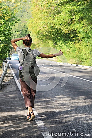 Young woman with backpack behind her back tries to stop passing car to hitchhike Stock Photo