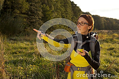 Young woman with backpack in a meadow showing way . Hiking at summertime. Geocaching Stock Photo