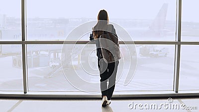 Young woman with backpack near terminal window. Caucasian female tourist using smartphone in airport lounge. Travel. 4K. Stock Photo