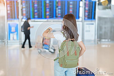 Young woman with bag and luggage checking flight time information board in international airport, before check in. Travel, Stock Photo