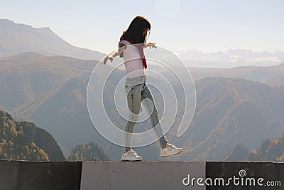 Young woman balancing on the edge of an abyss walks along the road parapet Stock Photo