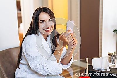 Young woman in bathrobe in hotel room using mobile phone Stock Photo