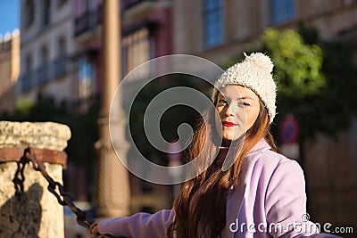 Young woman, beautiful, straight brown hair, sweater, coat and wool hat, supported by a large chain, with a sensual and Stock Photo