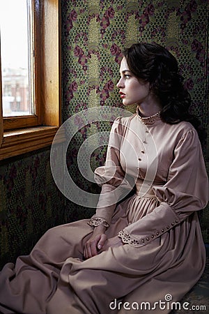 Young woman in beige vintage dress of early 20th century sitting Stock Photo
