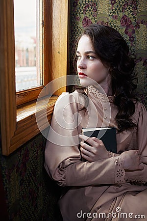 Young woman in beige vintage dress of early 20th century sitting Stock Photo